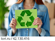 Thoughtful young woman showing a green recycling symbol made of paper in her hands to promote the concept of recycling and environmental protection. Стоковое AI-изображение, AI-художник Оксана Гильман / Фотобанк Лори