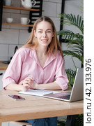 Young woman writing, taking notes, female student smiling sitting with laptop. Стоковое фото, фотограф Оксана Гильман / Фотобанк Лори