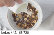 Dry breakfast cereals in a white bowl pour the milk and mix, chocolate and corn flakes, a healthy meal. Стоковое видео, видеограф Глущенко Елена / Фотобанк Лори