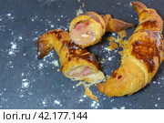 Croissant cut open revealing layers and ham and cheese filling with a shiny glaze, Sliced ham-filled croissant on a slate background sprinkled with flour, homemade croissant. Стоковое фото, фотограф carlos l vives / Фотобанк Лори