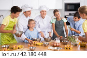 During cooking lesson, female cook tells children about culinary rules, guy assistant helps child. Стоковое фото, фотограф Яков Филимонов / Фотобанк Лори