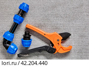 Ratcheting pipe cutter with fittings for HDPE pipes with an angle, coupling and threaded adapter equipped with compression clamp with collet, lie on gray surface. Стоковое фото, фотограф Владимир Григорьев / Фотобанк Лори