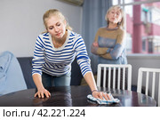 Elderly mother is unhappy with the way her adult daughter dusts the table in room. Стоковое фото, фотограф Яков Филимонов / Фотобанк Лори