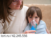 A mother woman with an inhaler helps her child cope with the disease. Inhalation for a sick asthmatic child to treat allergies. Стоковое фото, фотограф Андрей Журавлев / Фотобанк Лори