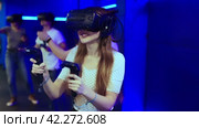 Cheerful emotional young woman in VR headset fully immersed in game, actively engaged in virtual reality world, manipulating objects or shooting targets with joysticks in hands. Стоковое видео, видеограф Яков Филимонов / Фотобанк Лори