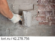 a man with a trowel in his hands plasters an old brick wall with a cement-sand mixture. Home repairs. Стоковое фото, фотограф Коханова Наталья / Фотобанк Лори