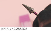 A specialist holds in his hands a carbide cutter for hardware manicure with a red notch on a pink background with copy space. Стоковое видео, видеограф Сергей Чайко / Фотобанк Лори