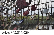 Multi-coloured love locks on the fence of the bridge over the river. The padlocks symbolise unbreakable love. Love locks that decorate many bridges around the world. Close-up. Стоковое видео, видеограф Воловодов Владимир / Фотобанк Лори
