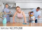 Dreamy teenage girl wiping table while cleaning house with family. Стоковое фото, фотограф Яков Филимонов / Фотобанк Лори