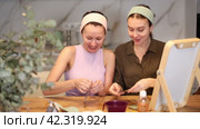 Two close female friends wearing matching headbands sitting at home table and looking in vanity mirror while discussing and comparing hydrogel patches for under-eye skin care. Стоковое видео, видеограф Яков Филимонов / Фотобанк Лори