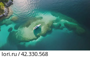 Yacht in open sea near the shore, top view from above. Anchorage of a large catamaran on transparent ocean water. Beautiful rocky beach with sailing boat. Стоковое AI-видео, аниматор Igor Tichonow / Фотобанк Лори