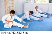 Young jiu-jitsu fighter stretching before group martial arts training. Стоковое фото, фотограф Яков Филимонов / Фотобанк Лори