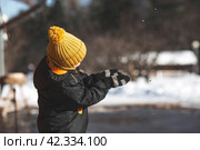 Portrait of a little boy in a yellow hat. The child runs through puddles on the farm, has fun and plays. It's a sunny day. Early spring. The first drop. Стоковое фото, фотограф Photojuli / Фотобанк Лори