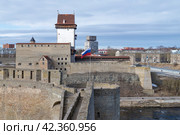 Российский флаг в Ивангородской крепости на фоне замка Германа (Нарва, Эстония) мартовским днем. Граница России и Эстонии (2024 год). Стоковое фото, фотограф Виктор Карасев / Фотобанк Лори