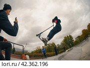 Moscow, Russia - August 27, 2019: Teenager performs a trick on sportive push scooter on a city sports ground. He jumping. Extreme sports is very popular. Редакционное фото, фотограф YuryKara / Фотобанк Лори