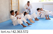 Multinational group of focused teenagers in white kimono performing core twist exercise with simultaneous punches during martial arts training session under guidance of experienced adult coach. Стоковое видео, видеограф Яков Филимонов / Фотобанк Лори