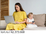 Unplugging mother after work. Child using mobile phone while mom working remotly at home. Стоковое фото, фотограф Natalia Gdovskaia / Фотобанк Лори