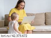 Mother working on laptop during quarantine. Homelife distractions. Curious baby looking at display. Стоковое фото, фотограф Natalia Gdovskaia / Фотобанк Лори