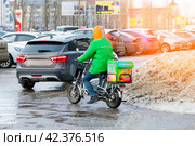 A courier of the Sbermarket delivery service on an electric bicycle delivers pre-ordered food or goods to a client (2024 год). Редакционное фото, фотограф Антон Вахрушев / Фотобанк Лори
