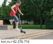 Moscow, Russia - July 26, 2019: Push scooter stunts on the city sport ground in the spring day. Boy showing trick. Healthy lifestyle. Extreme sports is popular among youth. Street photography. Редакционное фото, фотограф YuryKara / Фотобанк Лори