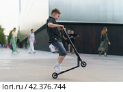 Moscow, Russia - July 26, 2019 Teenager ready to perform a trick at sportive push scooter on a city street. Редакционное фото, фотограф YuryKara / Фотобанк Лори