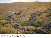 Квинстаун, Новая Зеландия - 30 декабря 2023 года. Авиалайнер Air New Zealand летит низко над серпантином, вьющимся через сухие холмистые холмы. Редакционное фото, фотограф Евгений Дробитько / Фотобанк Лори