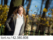 Красивая девушка со светло-каштановыми волосами стоит возле ствола дерева в аллее осеннего парка. Привлекательная молодая женщина в сером пальто и белом свитере. Осенний сезон. Стоковое фото, фотограф Андрей Степанов / Фотобанк Лори
