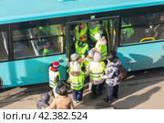 Группа детей в светоотражающих жилетах под присмотром взрослых сопровождающих заходит в автобус (2024 год). Редакционное фото, фотограф Станислав Кноп / Фотобанк Лори