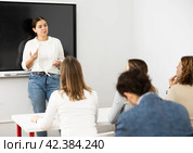 Young female teacher near interactive board, gesturing with hand in front of people sitting at desks in auditory. Стоковое фото, фотограф Яков Филимонов / Фотобанк Лори