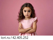 Serious funny little girl in pink dress arms crossed at pink backdrop, posing serious looking. Lovely kid lady coquette expressing emotion, studio shot. Child image emotion concept. Copy ad text space. Стоковое AI-изображение, AI-художник Aleksandr Golubev / Фотобанк Лори