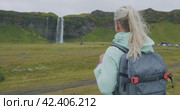 Woman with backpack enjoying impressive Seljalandsfoss waterfall in Iceland. Стоковое видео, видеограф Igor Tichonow / Фотобанк Лори