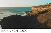 Rocky coastline alongside cliff, blue Atlantic Ocean water reflect at sunset. Nature landscape. Golden sandstone bluff beach. Tourists meet dusk. Travel destination. Fuerteventura Island, Canaries. (2022 год). Стоковое видео, видеограф Igor Tichonow / Фотобанк Лори