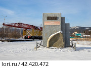 Памятник, посвящённый строителям Байкало-Амурской магистрали (БАМ). Город Северобайкальск, Республика Бурятия, Сибирь, Россия. На памятнике надписи: «1977» и «Слава первопроходцам БАМа». На дальнем плане путеукладчик-памятник (укладочный кран). Достопримечательности Северобайкальска. (2024 год). Редакционное фото, фотограф Андрей Степанов / Фотобанк Лори