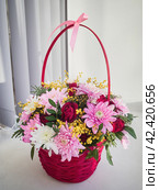 A beautiful bouquet of bright flowers in a wicker red basket stands on the window on a white background. Daylight . Happy Birthday, Valentine's Day, March 8th International Women's Day , Mother's Day. Стоковое фото, фотограф Светлана Семёновская / Фотобанк Лори