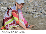 A teenage girl, wearing a cap and pareo, sits on a pebbled beach and looks into the camera. Стоковое фото, фотограф Светлана Семёновская / Фотобанк Лори