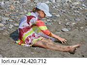 A teenage girl in a cap and a pareo is sitting on a pebble beach. Стоковое фото, фотограф Светлана Семёновская / Фотобанк Лори