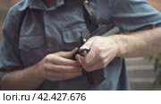 Young man dressed in a security guard uniform charges the gun into the holster close-up. Стоковое видео, видеограф EStarodubov / Фотобанк Лори