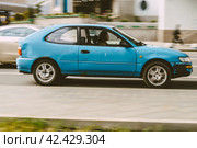 Blue old Toyota Corolla 3-door hatchback in motion on the city road. Woman driving rusty rumpled car. Fast moving vehicle with blurred background (2021 год). Редакционное фото, фотограф Константин Григорьев / Фотобанк Лори