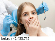 Closeup terrified girl woman scared at dentist visit, siting in chair, covering mouth, doesn't want dental procedure, drilling, tooth extraction, clinic office background. Fear of dentists. Toothache. Стоковое фото, фотограф Ирина Михайличенко / Фотобанк Лори