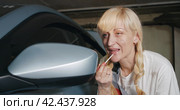 Автосервис. Attractive woman mechanic applying lipstick looking at car mirror in garage workshop. Стоковое видео, видеограф EStarodubov / Фотобанк Лори