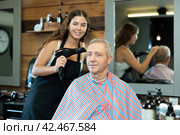 Girl hairdresser completes creation of haircut and dries hair with hairdryer to elderly male client. Стоковое фото, фотограф Яков Филимонов / Фотобанк Лори