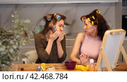 Two carefree adult besties sitting with colorful hair rollers on heads and applying golden hydrogel under-eye patches, enjoying self care and pampering moment at home together. Стоковое видео, видеограф Яков Филимонов / Фотобанк Лори