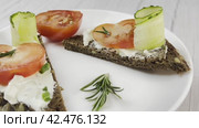 Sandwiches with cottage cheese and cucumber slices, cherry tomatoes are spinning on a white plate on a wooden table. Top view, side view. Стоковое видео, видеограф Ярославский Максим / Фотобанк Лори