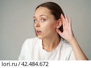 Young woman listening with her hand on an ear on gray background. Стоковое фото, фотограф Сергей Толмачёв / Фотобанк Лори