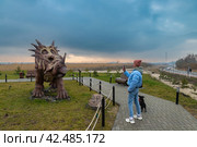 Девушка с собакой фотографирует фигуру стиракозавра в Динопарке Янтарного (2024 год). Редакционное фото, фотограф Константин Чижов / Фотобанк Лори