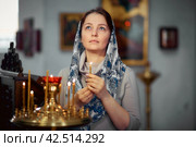 Lifestyle woman lights candles in the Church, praying in front of the icon. Стоковое фото, фотограф Арзюков Вадим Николаевич / Фотобанк Лори
