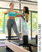 Attentive hispanic woman trainer controlling positive girl during training with resistance bands. Стоковое фото, фотограф Яков Филимонов / Фотобанк Лори