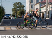 Father and son are riding around the city, riding bicycles. Middle-aged urban residents traveling by bike. People are driving along a pedestrian crossing in the city.Zaraisk, Russia, August 2023. Редакционное фото, фотограф Photojuli / Фотобанк Лори