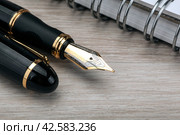 golden fountain pen near the notepad on a wooden table. Стоковое фото, фотограф Александр Калугин / Фотобанк Лори