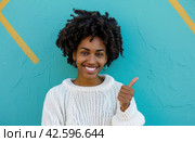 ctp afroamerican young woman in white sweater with thumbs up while pointing to right. Стоковое AI-изображение, AI-художник Юлия Гапеенко / Фотобанк Лори